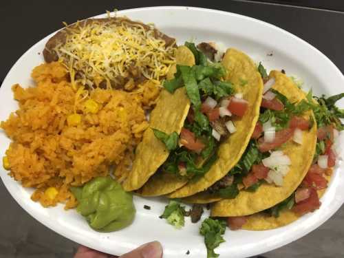 A plate of tacos with lettuce, tomatoes, and onions, served with rice, beans, and guacamole.