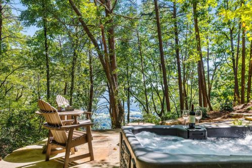 A hot tub surrounded by trees, with two chairs and a table, overlooking a scenic view.