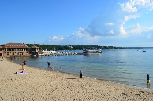 A sandy beach with people enjoying the sun, a docked boat, and a scenic view of the water and clouds.