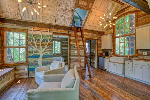 Cozy interior of a rustic cabin with wooden walls, large windows, and a ladder leading to a loft area.