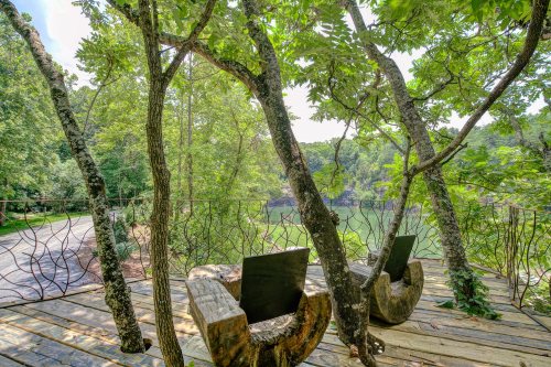 A serene outdoor seating area with wooden chairs surrounded by trees, overlooking a calm lake.