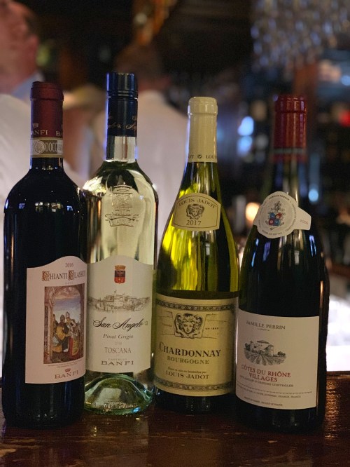 Four bottles of wine displayed on a bar: Chianti, a Tuscan white, Chardonnay, and Côtes du Rhône Villages.