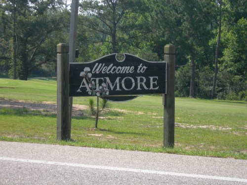 Sign reading "Welcome to Atmore" with a cotton plant design, set against a green landscape.