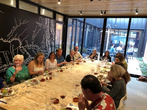 A group of people seated at a long table, enjoying drinks and food in a modern, well-lit dining space.
