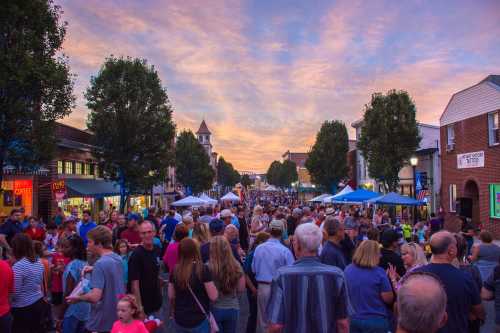 A bustling street filled with people enjoying an outdoor event at sunset, with tents and shops lining the road.