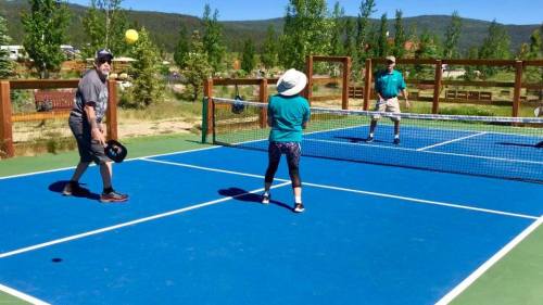 Two people playing pickleball on a blue court, with a third person watching in a scenic outdoor setting.