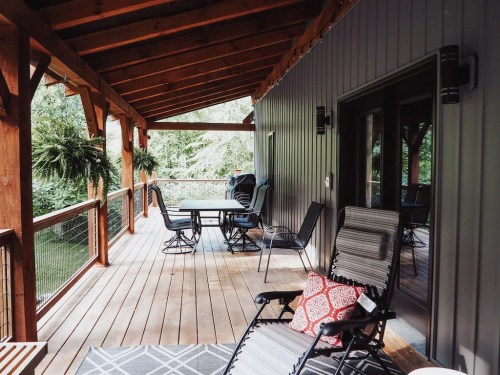 A cozy porch with wooden beams, chairs, and a table overlooking a serene outdoor view.