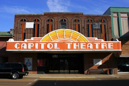 Historic Capitol Theatre facade with a bright marquee and brick exterior, featuring orange and yellow accents.