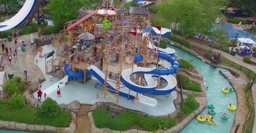 Aerial view of a water park featuring slides, a play structure, and a lazy river with people enjoying the attractions.