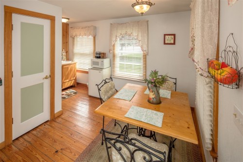 Cozy kitchen with a wooden table, chairs, and natural light from windows, featuring a microwave and decorative elements.