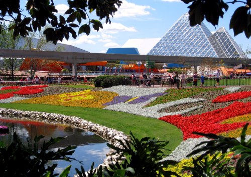 Colorful flower beds in a park with modern architecture in the background and a clear blue sky.