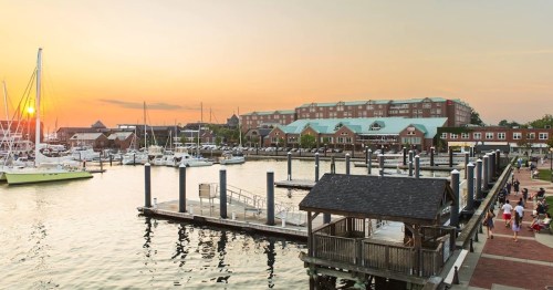 Sunset over a marina with boats, docks, and a waterfront building, creating a serene atmosphere.