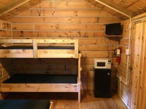 Interior of a wooden cabin featuring bunk beds, a microwave, a mini fridge, and a fire extinguisher on the wall.