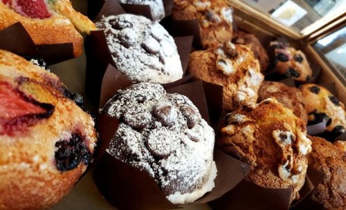 A variety of freshly baked muffins in brown paper liners, featuring fruits and chocolate.