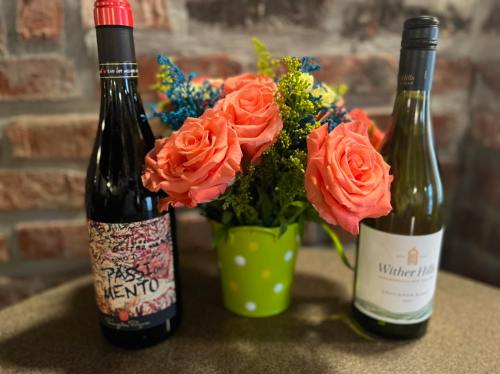 A vibrant bouquet of orange roses in a green polka dot vase, flanked by two bottles of wine on a textured surface.