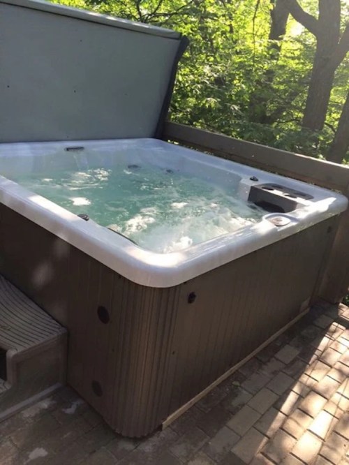 A hot tub with bubbling water, situated on a wooden deck surrounded by greenery.