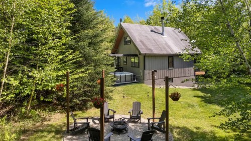 A cozy cabin surrounded by trees, featuring a fire pit and hot tub in a serene outdoor setting.