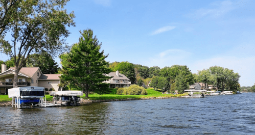 Scenic view of a lake with houses and docks along the shoreline, surrounded by trees under a clear blue sky.