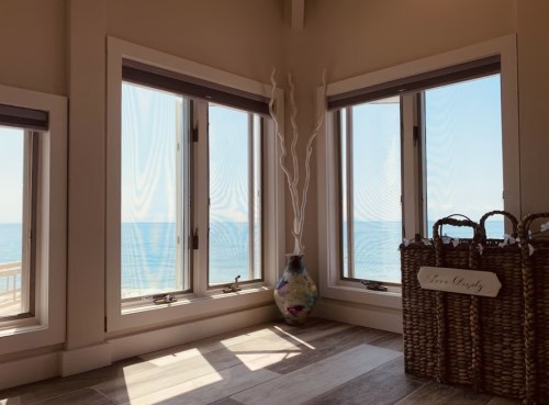 Bright room with large windows overlooking the ocean, featuring a decorative vase and woven baskets.