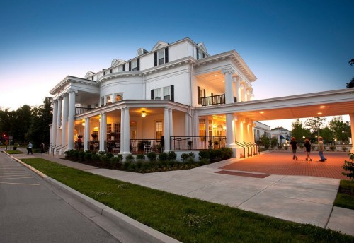A grand white building with columns, warmly lit at dusk, featuring a wide entrance and landscaped surroundings.