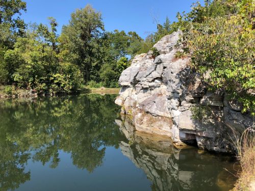 A serene lake surrounded by lush greenery and a rocky shoreline under a clear blue sky.