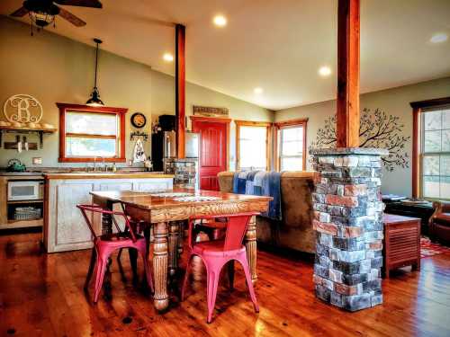 Cozy interior of a home featuring a wooden dining table, red chairs, stone pillars, and a bright living area.