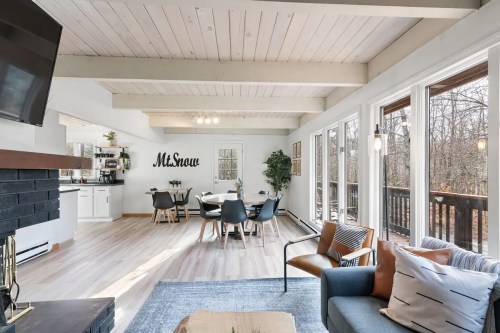 Bright, modern living space with a dining area, large windows, and wooden beams, featuring a cozy seating arrangement.