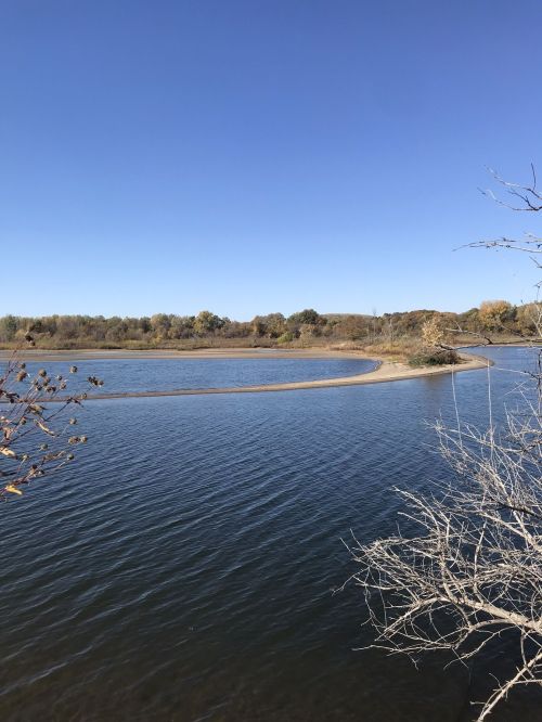 A serene river scene with a sandy curve, surrounded by trees under a clear blue sky.
