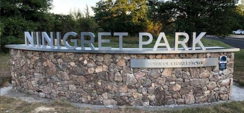 Sign for Ninigret Park in Charlestown, featuring a stone base and metal lettering, surrounded by greenery.