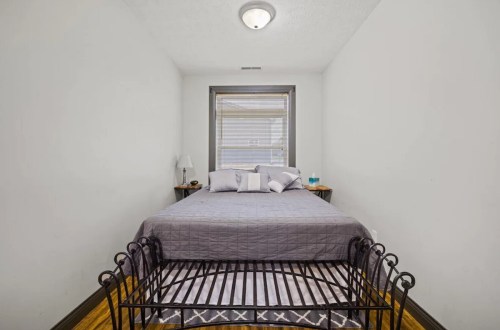 Cozy bedroom featuring a gray bedspread, bedside tables, and a window with blinds.