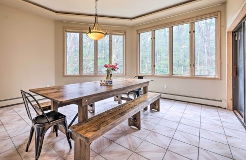 A spacious dining area with a wooden table, benches, and large windows overlooking a wooded view.