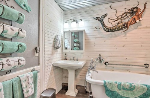 Cozy bathroom with a vintage tub, teal accents, and a mermaid wall decoration. Soft towels hang nearby.