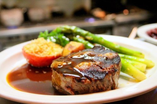 A plated meal featuring a grilled steak, asparagus, a baked tomato, and a side of sauce.