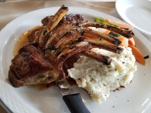 A plate featuring a rack of lamb with mashed potatoes and mixed vegetables on the side.