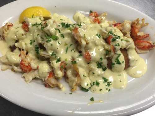 A plate of seafood topped with creamy sauce and garnished with parsley, served with a lemon wedge.