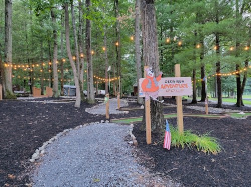 A pathway through a wooded area with string lights and a sign for Deer Run Adventure Golf.