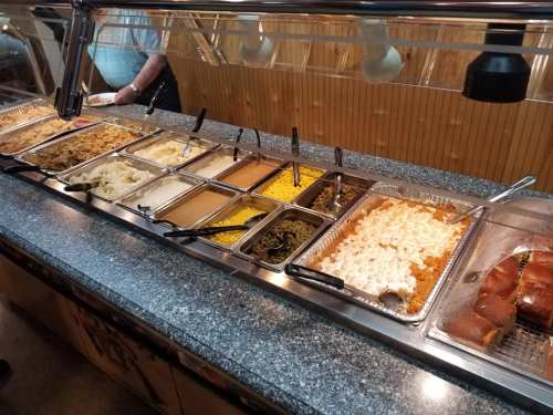 A buffet with various dishes including rice, mashed potatoes, corn, green beans, and rolls on a granite countertop.