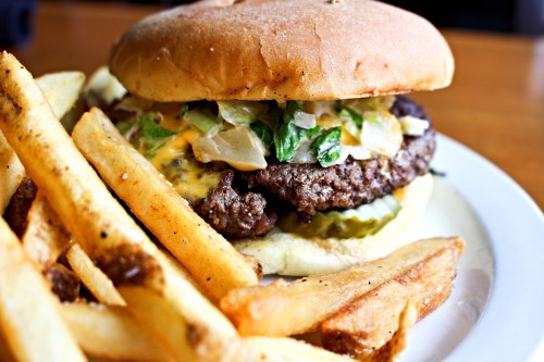 A juicy cheeseburger with lettuce, pickles, and onions, served with crispy French fries on a white plate.