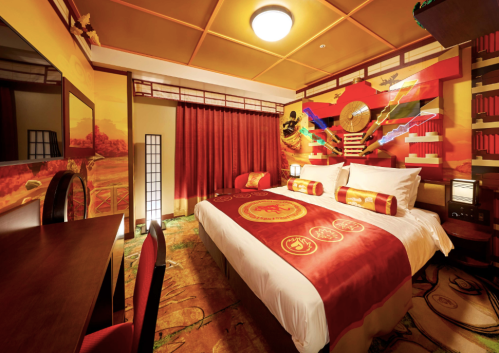 A vibrant hotel room featuring red and gold decor, a large bed, and traditional Japanese elements.
