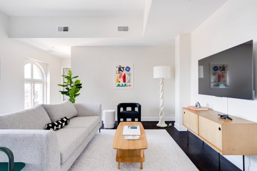 A modern living room featuring a gray sofa, wooden coffee table, TV, and decorative art on the walls.