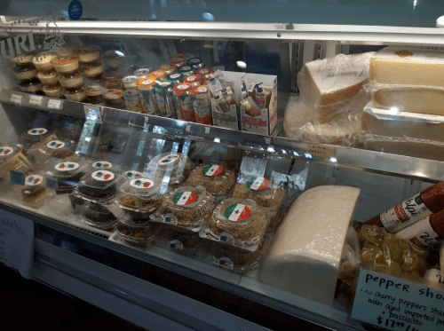 A display case filled with various packaged foods, including desserts, sauces, and cheeses, labeled with price tags.