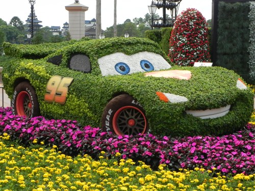 A topiary sculpture of a race car, covered in greenery and flowers, with a smiling face and the number 95.