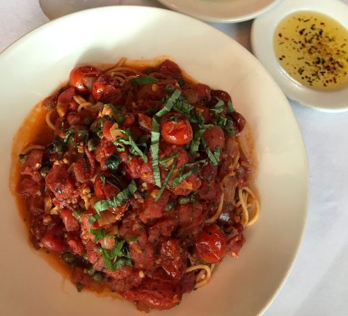 A plate of spaghetti with tomato sauce and basil, served with a glass of red wine, bread, and olive oil on the side.