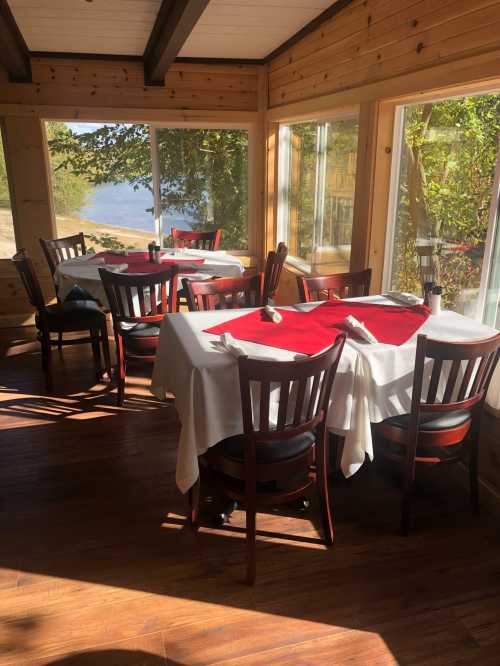 Cozy dining area with wooden tables and chairs, set with white tablecloths and red napkins, overlooking a scenic view.