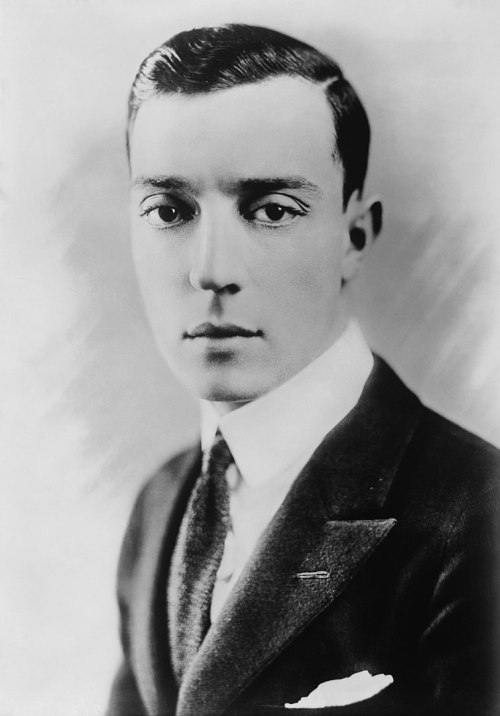 A black and white portrait of a young man in a suit, with slicked-back hair and a serious expression.