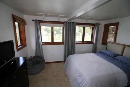 A cozy bedroom with a bed, dresser, and large windows overlooking a scenic view. Soft lighting and neutral decor.