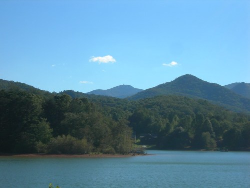 A serene lake surrounded by lush green mountains under a clear blue sky with a few clouds.