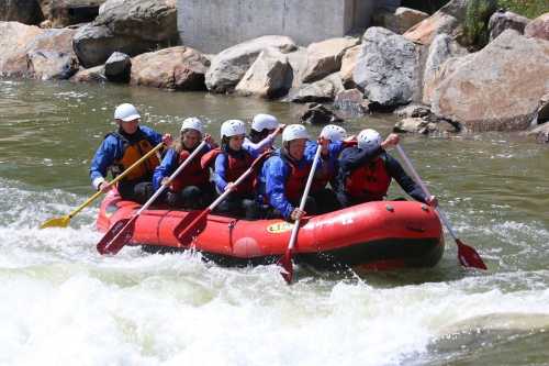 A group of six people in a red raft navigating whitewater rapids, wearing helmets and life jackets.