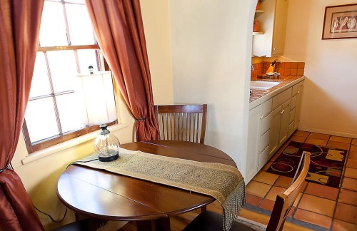 Cozy kitchen nook with a round table, two chairs, a lamp, and a view of the kitchen area with warm-toned decor.