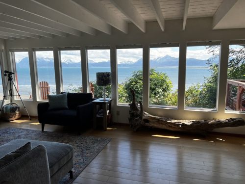Cozy living room with large windows showcasing a scenic view of mountains and water, featuring a sofa and natural decor.